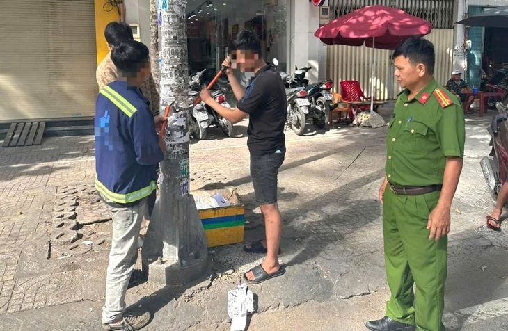 Ba thanh niên bị buộc cạo sạch quảng cáo dán 'chui' trên cột điện- Ảnh 1. Ba người đang làm sạch một trụ điện trên đường Trần Hưng Đạo (quận 5) - Ảnh: A.X.